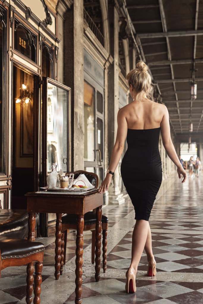 A gorgeous woman wearing a black dress in a vintage Italian cafe